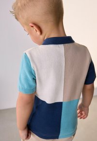 Stickad polo med kort ärm, som har färgblock i ljusblått, marinblått, beige och krämfärgat; slät textur; ribbat krage och manschetter.
