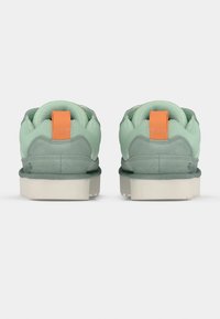 Baskets vertes avec une empeigne en mesh texturé, semelle en caoutchouc, col rembourré et languette orange au talon. Matériaux doux et design robuste.