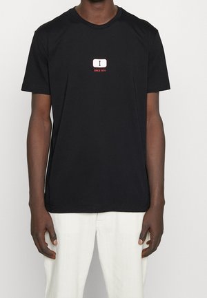 Black cotton t-shirt featuring a central white rectangular logo with "I" and "SINCE 1974" in red text. Simple crew neck design.