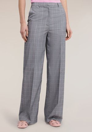 Pantalones anchos de cuadros grises combinados con una blusa rosa y bailarinas rosas adornadas, posando frente a un fondo neutro.