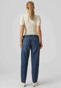 Blå denimjeans med avslappnad passform, med en smockad midja och bakfickor, kombinerat med en vit ribbad topp och beige sneakers.