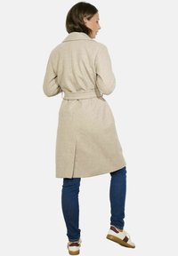 Šviesiai rudas vilnos mišinys paltas su diržu juosmens srityje, apykakle ir nugaros ventiliacija. Suderintas su mėlynomis džinsinėmis kelnėmis ir daugiaspalviais batais.