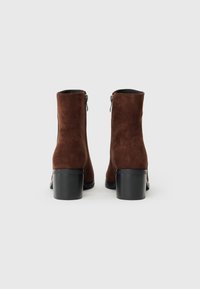 Braune Wildleder-Ankle Boots mit einem gestapelten Absatz, seitlichem Reißverschluss und glattem Innenfutter. Einfaches Design mit strukturierter Oberfläche.