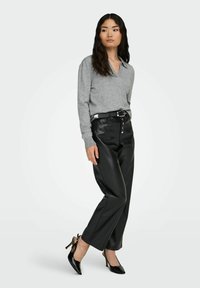 Grauer Strickpullover mit V-Ausschnitt, kombiniert mit schwarzen, aus Kunstleder gefertigten Hosen mit Knopfverschluss und einem schwarzen Gürtel. Schwarze High Heels runden das Outfit ab.