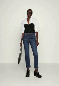Top preto justo sobre uma camisa branca, jeans azul de perna reta, sapatos plataforma pretos e óculos de sol. Design simples e elegante. Bolsa preta.