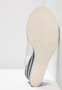 Sandale blanche à bout ouvert avec une semelle texturée, présentant un design côtelé gris clair et bleu marine sur la bride et un talon courbé.