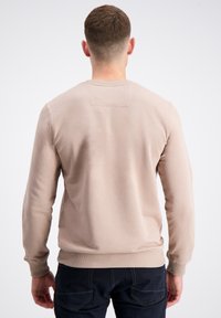 Felpa beige con maniche lunghe, scollatura rotonda, tessuto testurizzato e polsini e orlo a coste. Design minimalista con una piccola etichetta sul retro.