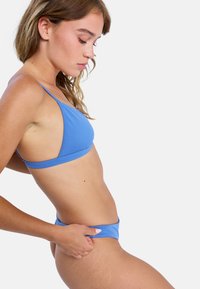 Ensemble bikini bleu comprenant un haut triangle et un bas taille basse, fabriqué en tissu lisse avec des bretelles fines et des détails de coutures minimalistes.