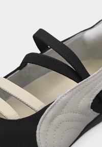 Κοντινό πλάνο ασπρόμαυρης μπαλαρίνας με ελαστικές λουρίδες που διασταυρώνονται στην επάνω πλευρά και ραφές καπιτονέ στην πλευρική επιφάνεια.