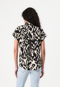 Chemise à manches courtes avec un imprimé léopard abstrait noir et crème, dotée d'un col boutonné et d'une coupe décontractée. Texture de tissu lisse.