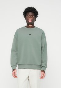 Green sweatshirt with a rounded neckline and ribbed cuffs; features a black 'BOSS' logo on the chest; made of soft material.
