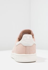 Ljusrosa mocka Adidas Stan Smith-sneakers sedda bakifrån med vit hältab och logotyp samt vit texturerad sula.