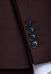 Ciemnoczerwony żakiet z delikatnym wzorem w kratkę, cztery czarne guziki na mankiecie oraz widoczne detale szycia.