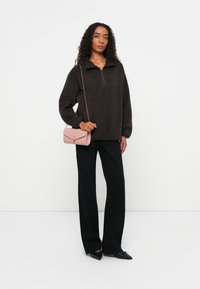 Bruine fleece pullover met een halve rits kraag, gecombineerd met zwarte wijde broek en een roze gestructureerde schoudertas. Zwarte schoenen maken de look compleet.