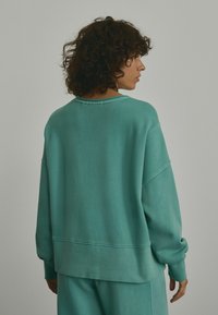 Mintgrüner Oversized-Pullover mit rundem Ausschnitt, überschnittenen Schultern und gerippten Bündchen. Weiche Textur, minimalistisches Design.