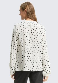 Weiße Bluse mit schwarzen Polka-Dots, langen Ärmeln und einem gerafften Ausschnitt. Weicher Stoff mit lockerem Schnitt.
