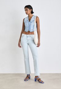 Svetlo modra kratka denim jakna z gumbi, v kombinaciji s svetlo modrimi ravnimi kavbojkami. Model nosi sandale na blok peto v modri in črni barvi.