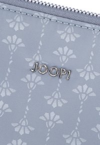Borsetta azzurra chiara realizzata in tessuto testurizzato con un motivo floreale. Logo argento "JOOP!" ben visibile sulla parte frontale.