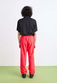 Sort kortærmet skjorte parret med lyserøde elastiske bukser. Sorte sneakers fuldender outfittet. Minimalistisk design.