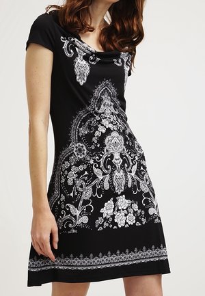 Sort kjole med korte ærmer, der har intrikate hvide blomster- og paisleymønstre, en draperet halsudskæring og en svajende skirt.