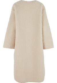 Bēša flīsa mētelis, garš un plaša silueta, ar teksturētu virsmu. Ar nokarenām plecu līnijām un apaļu kakla izgriezumu. Nav redzamu aizdares elementu.