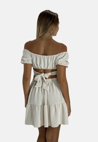 Leichtes beige Off-Shoulder-Kleid mit gestuftem Rock, elastischem Band am oberen Rand und einer Schleifen-Detail hinten. Texturiertes Material.