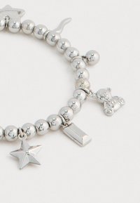Ασημένιο βραχιόλι με χάντρες, διακοσμημένο με charms σε σχήμα αστεριού, ράβδου και αρκουδάκι, σε ανοιχτό φόντο.