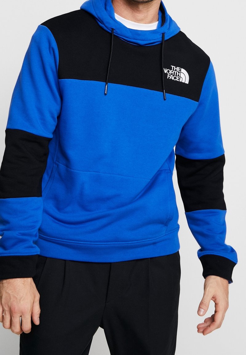 Hoodie v barevném blokování v modré a černé. Vyrobeno z měkké tkaniny, s klokaní kapsou, nastavitelnou kapucí a logem na hrudi.