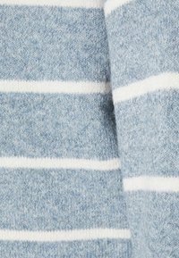 Vaaleansininen neulottu kangas, jossa on valkoisia vaakasuoria raitoja, näyttää yksityiskohtaisen tekstuurin ja pehmeän villamateriaalin lähikuvassa.