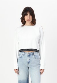 Witte cropped sweatshirt met lange mouwen, voorzien van schouderuitsparingen en een zwarte elastische tailleband met de tekst "KARL LAGERFELD JEANS".