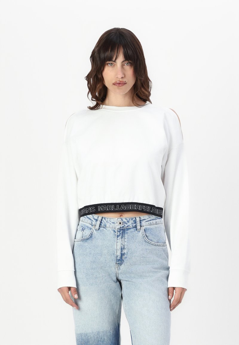 Witte cropped sweatshirt met lange mouwen, voorzien van schouderuitsparingen en een zwarte elastische tailleband met de tekst "KARL LAGERFELD JEANS".