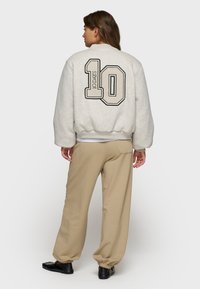 Sweatshirt gris clair avec un graphique noir "10 DAYS", des poignets côtelés et une coupe cropped, associé à un jogging beige et des chaussures noires.