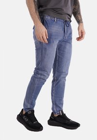 Pantaloni jogger in denim blu chiaro con vita elasticizzata e cordino. Indossati con sneakers nere caratterizzate da una superficie testurizzata.