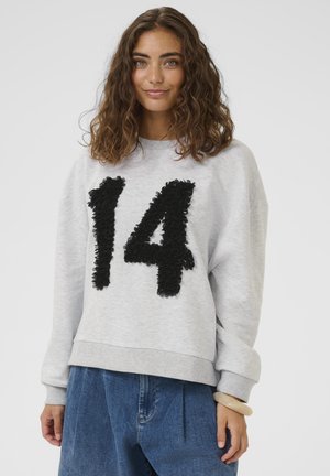 Siva majica z okrolim izrezom in spuščenimi rameni, na sprednji strani ima teksturirano črno številko "14". Kombinirana z ohlapnimi modrimi kavbojkami.