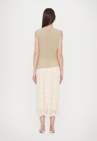 Top beige senza maniche con vestibilità ampia, abbinato a una gonna midi in crema all'uncinetto con motivi circolari e orlo a scallop.