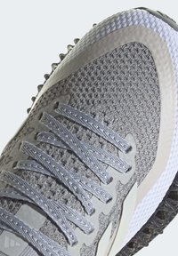 Scarpa sportiva grigia con una parte superiore in mesh testurizzato, dettagli in gomma e una suola sagomata con battistrada pronunciato per una migliore aderenza. Sei occhielli per i lacci.