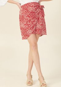 Gonna avvolgente rossa con motivi floreali e swirl bianchi, legata in vita. Tessuto leggero, design lungo fino al ginocchio.