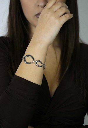 Silberarmband aus miteinander verbundenen ovalen und runden Formen, mit polierter Oberfläche und elegantem Design. Getragen am Handgelenk.