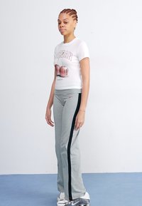 T-shirt blanc avec impression graphique, associé à un pantalon de survêtement gris avec une bande latérale noire, et des baskets argentées au design élégant.