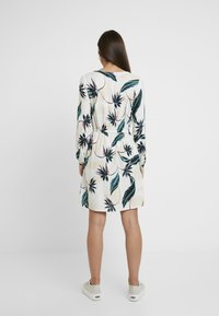 Kleid mit Blumenmuster aus leichtem Stoff, mit langen Ärmeln, tailliertem Schnitt und einer sanften Farbpalette in Grün- und Beigetönen.