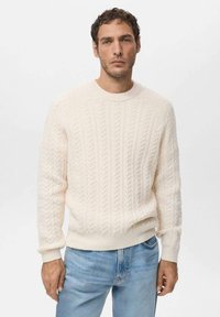 Maglione crema a trecce con maniche lunghe e scollo rotondo, abbinato a jeans azzurri. Tessuto morbido e vestibilità regolare.