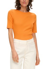 Pomarańczowy, dopasowany top z krótkim rękawem, wykonany z prążkowanej bawełny, w zestawieniu z jasnymi, wysokimi dżinsami. Prosty dekolt i czysty design.