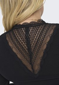 Black top featuring a lace back with intricate geometric patterns, scalloped edges, and a partial see-through design.