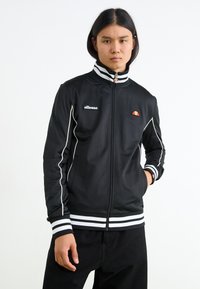 Sort lynlåsjakke med hvide accenter og stribede manchetter. Har logo på brystet og høj krave. Glat stof med et sporty design.