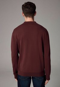 Burgundy kötött pulóver, gallérral, hosszú ujjal és bordázott aljjal. Az anyaga simának tűnik, puha tapintással.