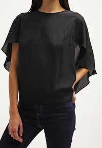 Sort bluse med korte ærmer har en glat satinfinish, løs pasform og flydende kappe-agtige ærmer. Inkluderer en lille lomme.