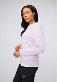 Lichtpaars sweatshirt met een ronde hals en geribbelde manchetten, gecombineerd met zwarte broek met een dierenlogo op de dij. Eenvoudig ontwerp.