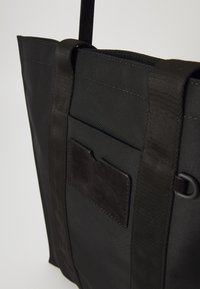 Černá taška přes rameno vyrobená z odolné tkaniny. Vybavena robustními popruhy, přední kapsou s semišovým akcentem a elegantním, jednoduchým designem.