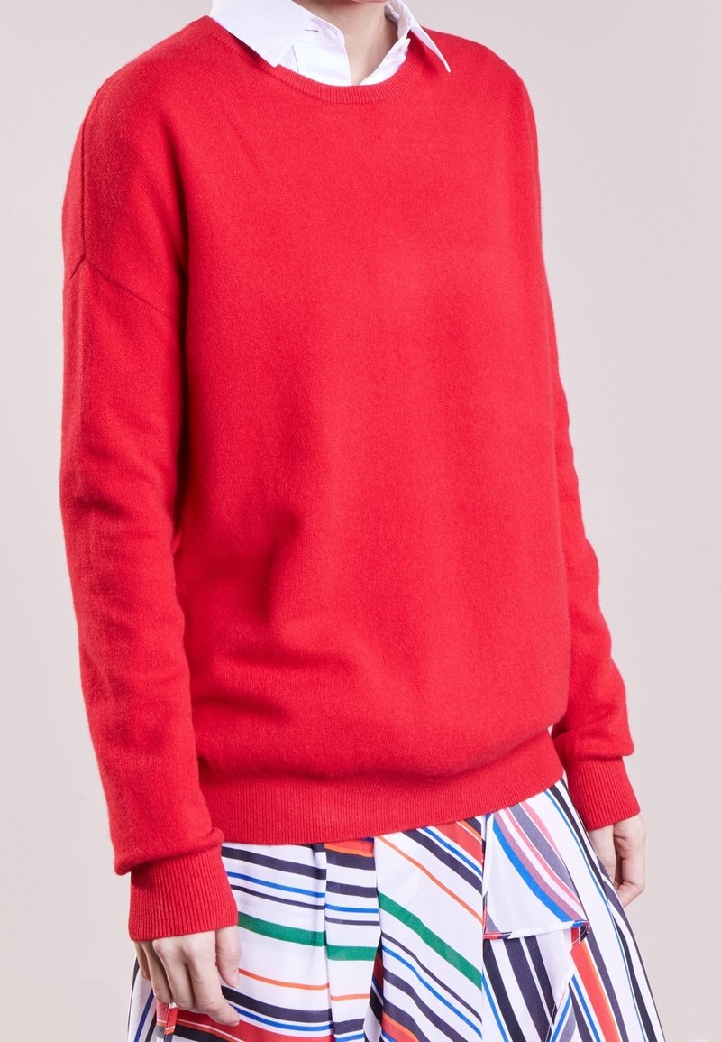 Suéter rojo hecho de material suave, con cuello redondo, mangas largas y puños y dobladillo de canalé. Combinado con una falda a rayas colorida.