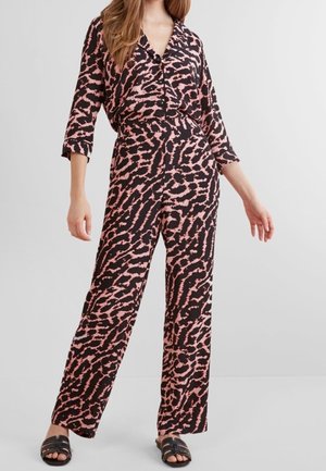 Woman wearing a loose-fit jumpsuit with a pink and black abstract animal print, featuring a V-neck and wide-leg pants, paired with black slide sandals.